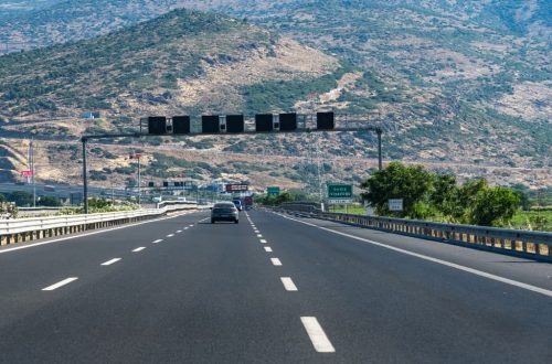 Long highway with cars traversing through rocky hills under blue skies, perfect travel scene.